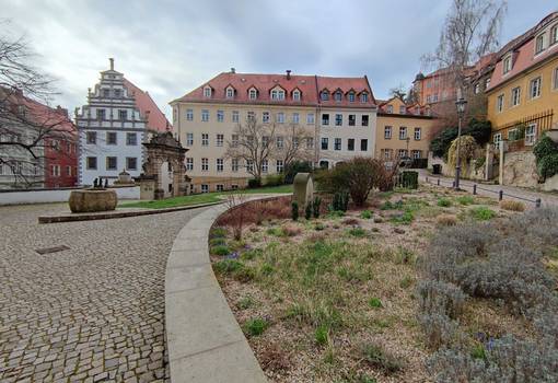 Grüner Platz mit Wegen, Beeten, historischem Stadttor und Giebelbau der Renaissance
